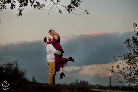 A couple was photographed in Forest Park St. Louis with the sky behind them, with the man picking the woman up with her feet off the ground