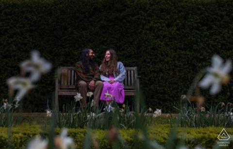The engaged couple's portrait at Ashbridge House Gardens in the United Kingdom was made memorable with a simple park bench element layered with a vibrant foreground of spring flowers