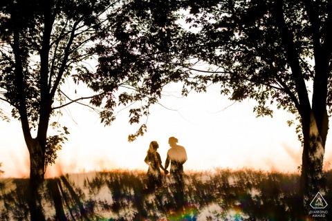 In the Kansas countryside, the couple walked hand in hand through the field, silhouetted against the sunset on the grass.