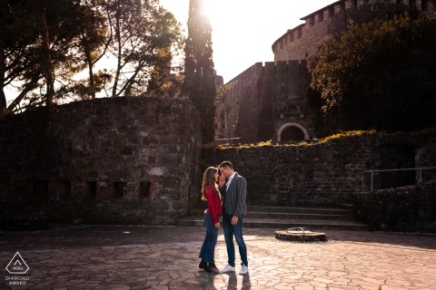 In Gorizia, Italy, he gently kisses her hand as they stand face to face against the backdrop of a historic castle, capturing a beautiful session before their wedding.